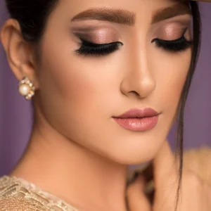 Close-up of woman with glamorous makeup and voluminous eyelash extensions, featuring soft shimmer eyeshadow and perfectly shaped brows against a blurred background.